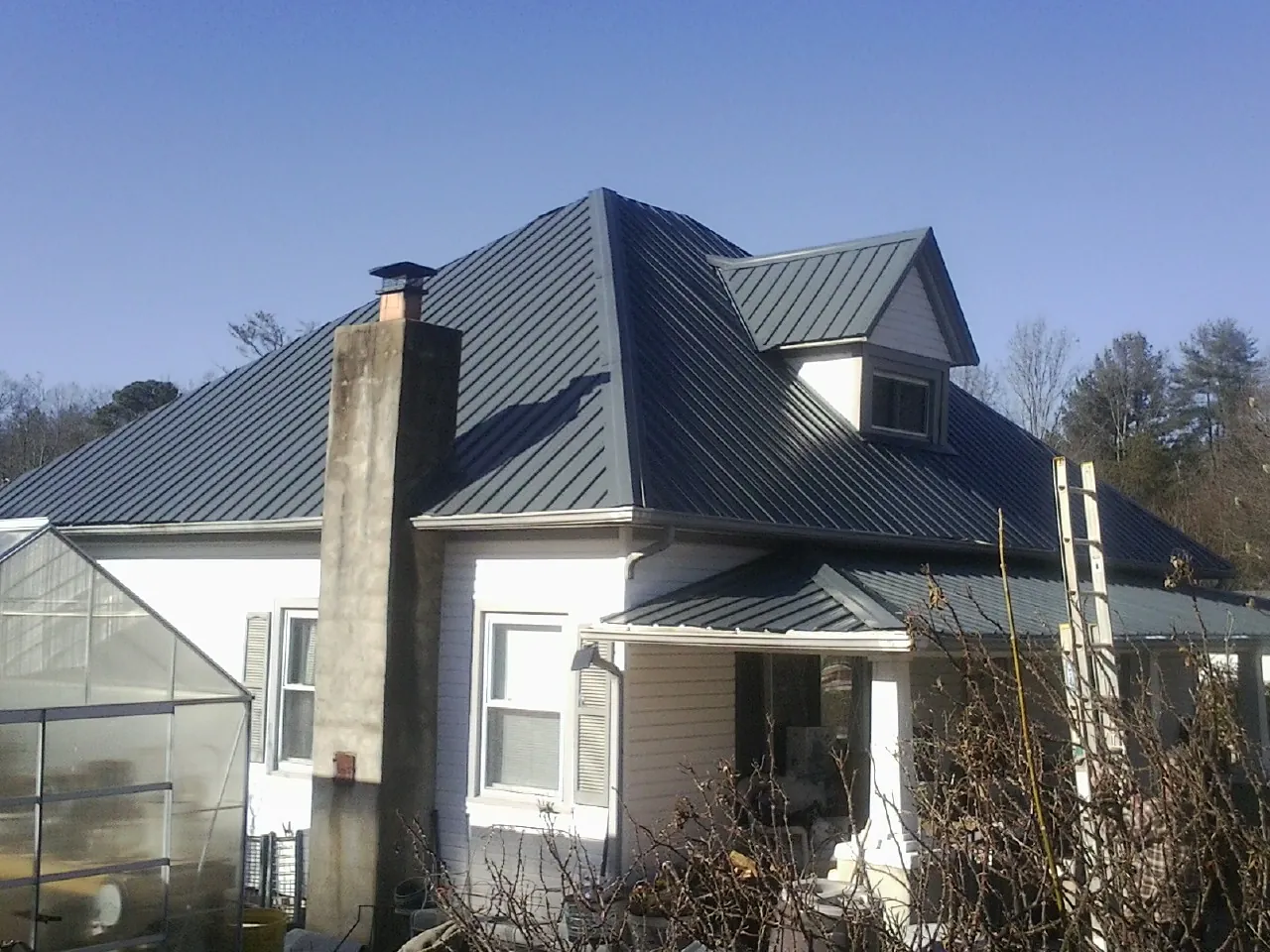 Dark blue standing seam metal roof on a white farmhouse with dormer — Slate & Tile Roof Repair by Roofing Brothers in Peapack