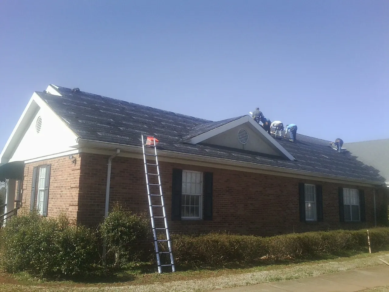 Crew tearing shingles off a brick ranch roof with a ladder set — Metal Roof Repair work by our crew in Peapack