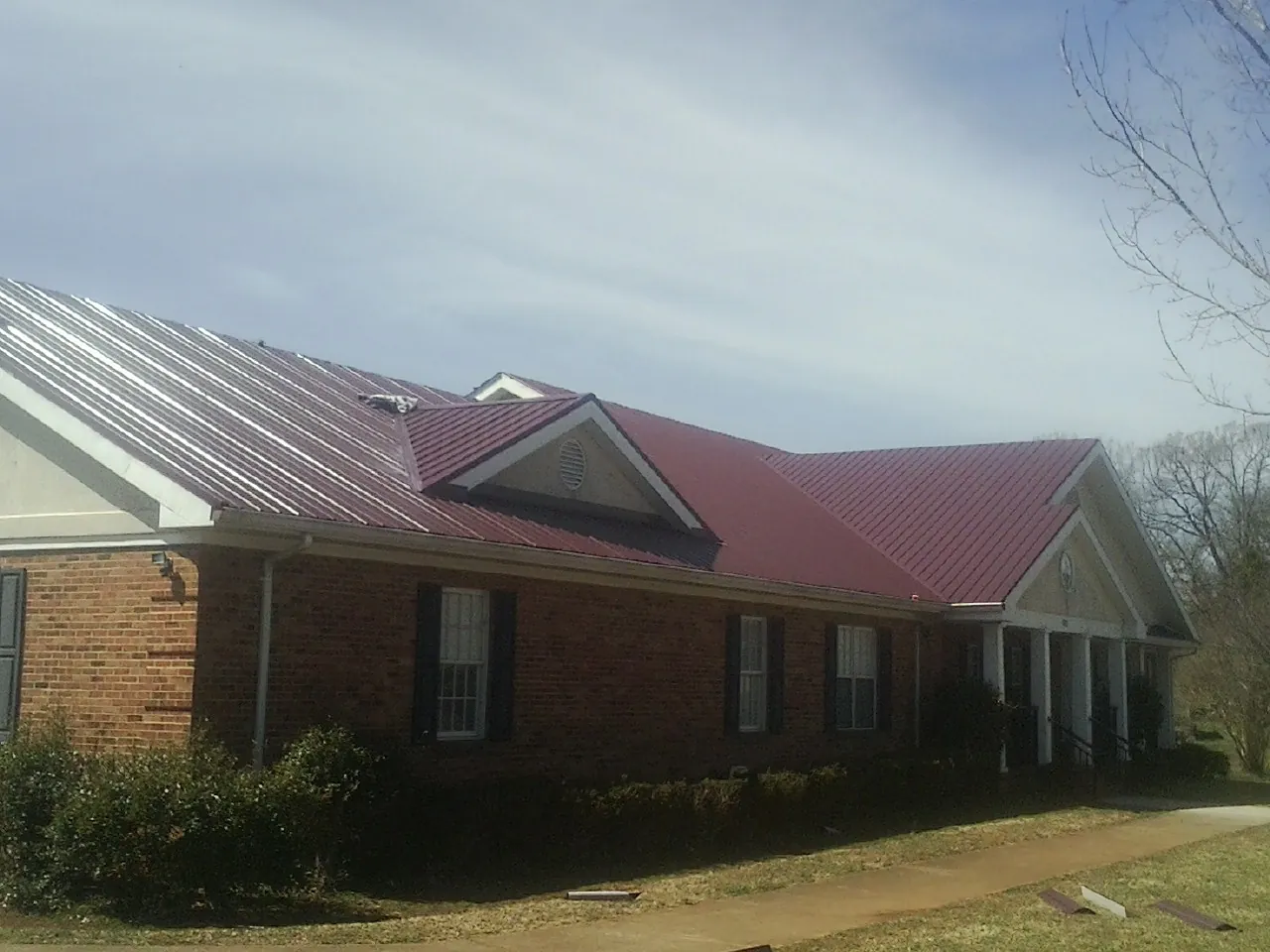 Red metal roof with gabled entries on a long brick building, from a Hail Damage Roof Repair job in Peapack