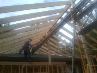 Rafters going up over a new addition with a worker on the wall in Peapack