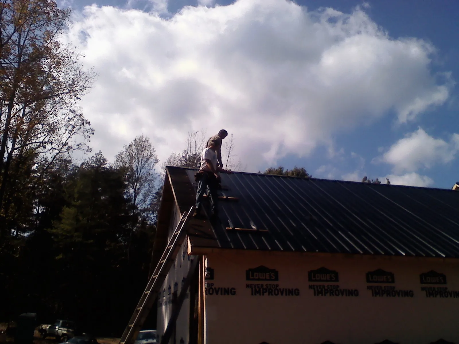 Roofer fastening dark metal panels high against a cloudy sky, from a Roof Inspection job in Peapack