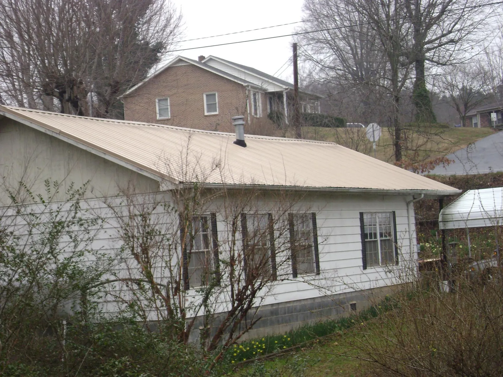 Tan metal roof on a white sided house set into a hillside — Commercial Roofing by Roofing Brothers in Peapack